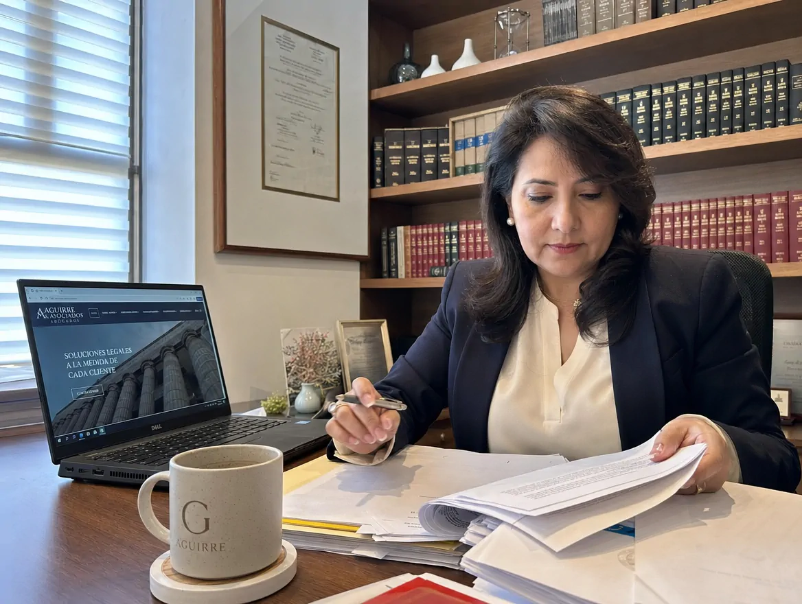 Abogada salvadoreña revisa documentos en su despacho con el sitio web de su firma